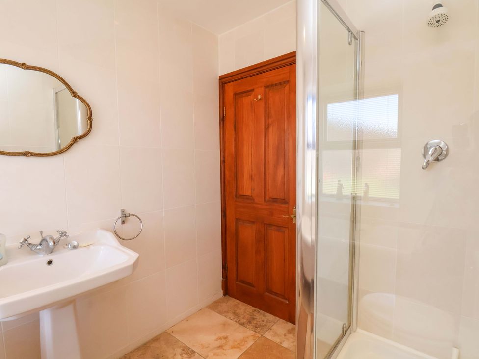 A bathroom with a sink, mirror, shower and door at 4 Cliff Cottages Port Mulgrave near Staithes