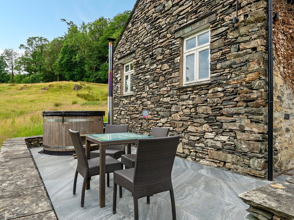 An outdoor seating area with a hot tub and a table with chairs at Dove Cottage at the Graythwaite Estate near Hawkshead