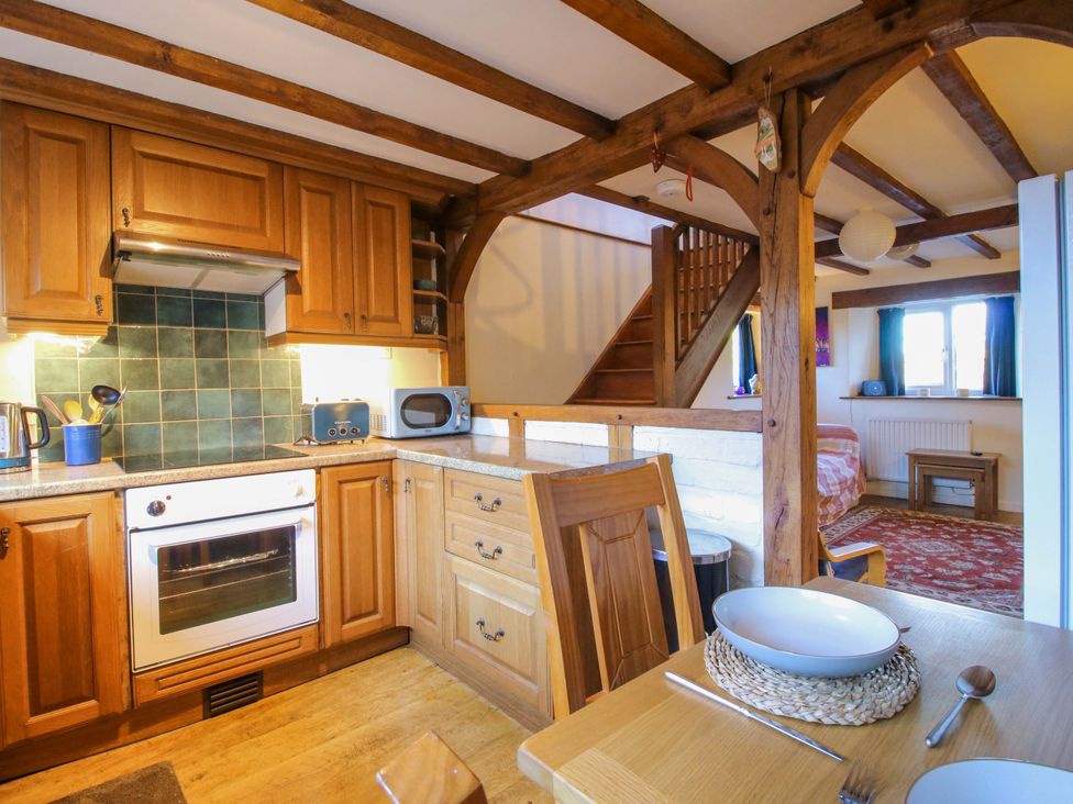 A kitchen with wooden cabinets and a dining area at Marigold Cottage in Clun near Bishop's Castle