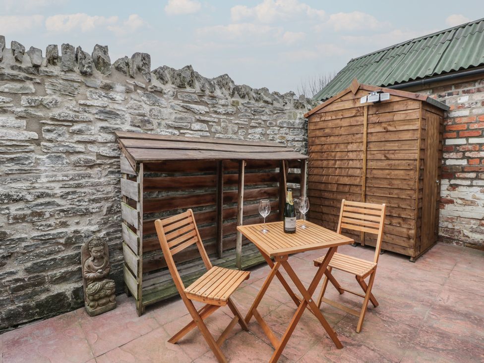 An outdoor space with a table and chairs next to a stone wall at Marigold Cottage in Clun near Bishop's Castle