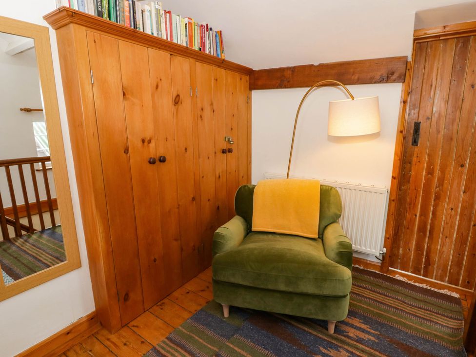 A snug with an armchair and bookshelf at Marigold Cottage in Clun near Bishop's Castle