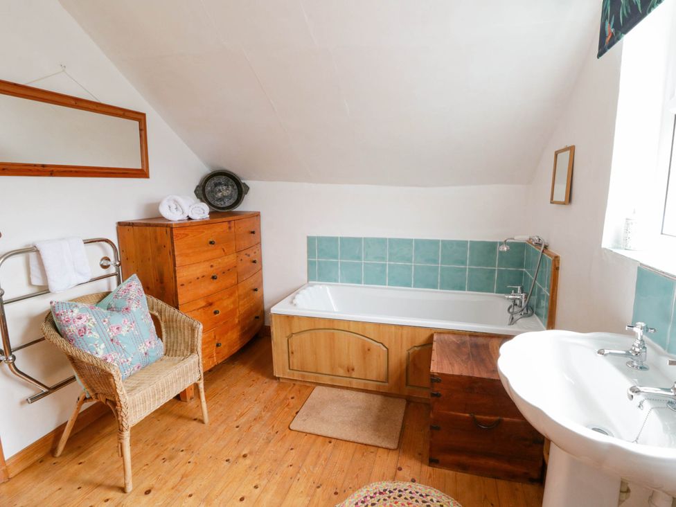 A bathroom with a bathtub, sink, and wooden storage at Marigold Cottage Clun near Bishop's Castle