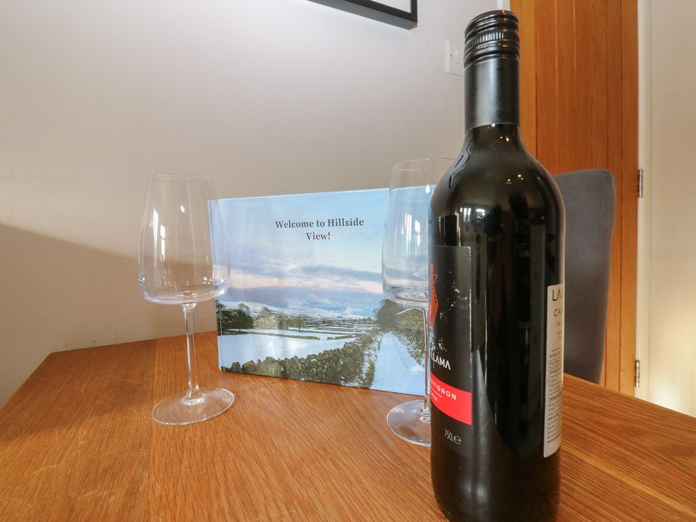 A dining table with a wine bottle and glasses at Hillside View in Hawes