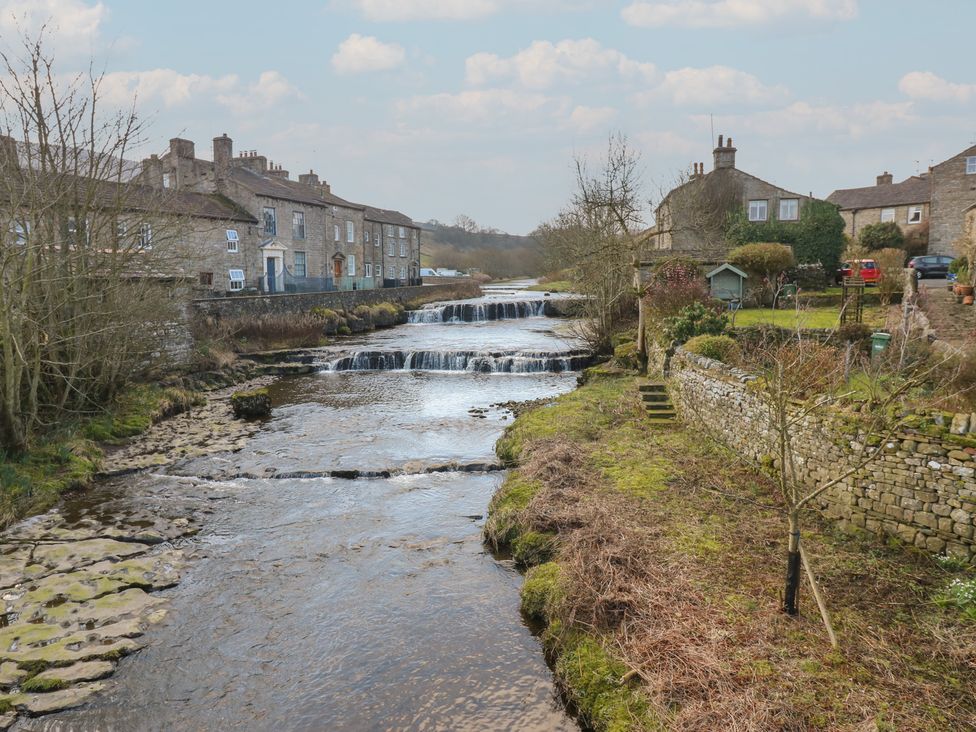 A waterfall and river with houses along the bank at Hillside View in Hawes