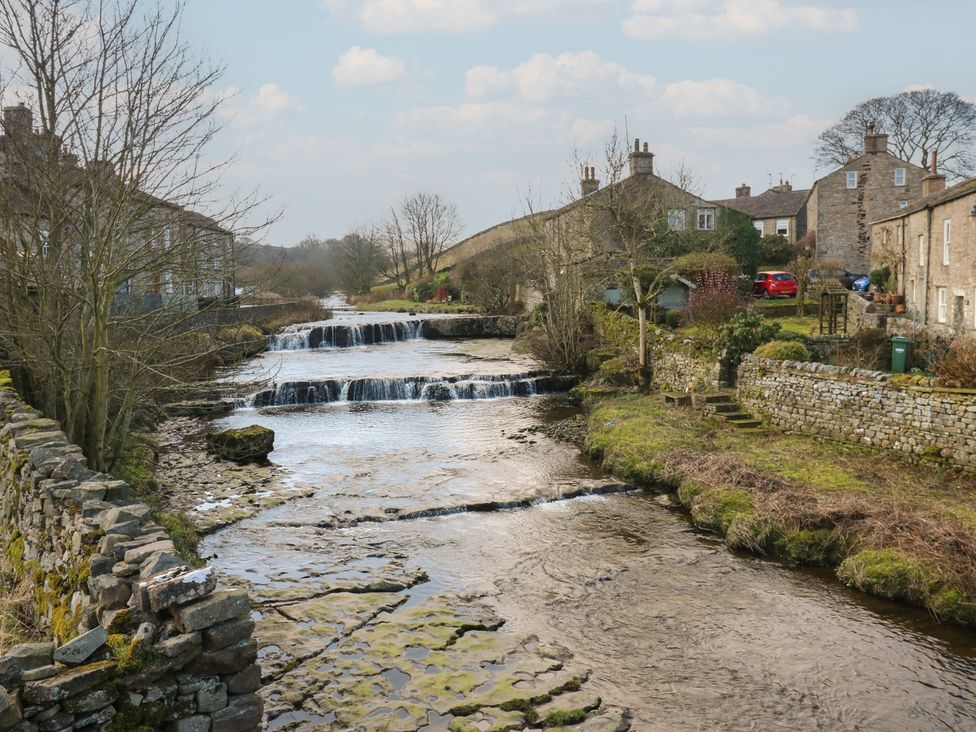 A stream with a waterfall and stone buildings at Hillside View in Hawes