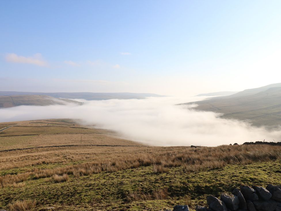 A valley covered in fog with hills in the background at Hillside View, Hawes