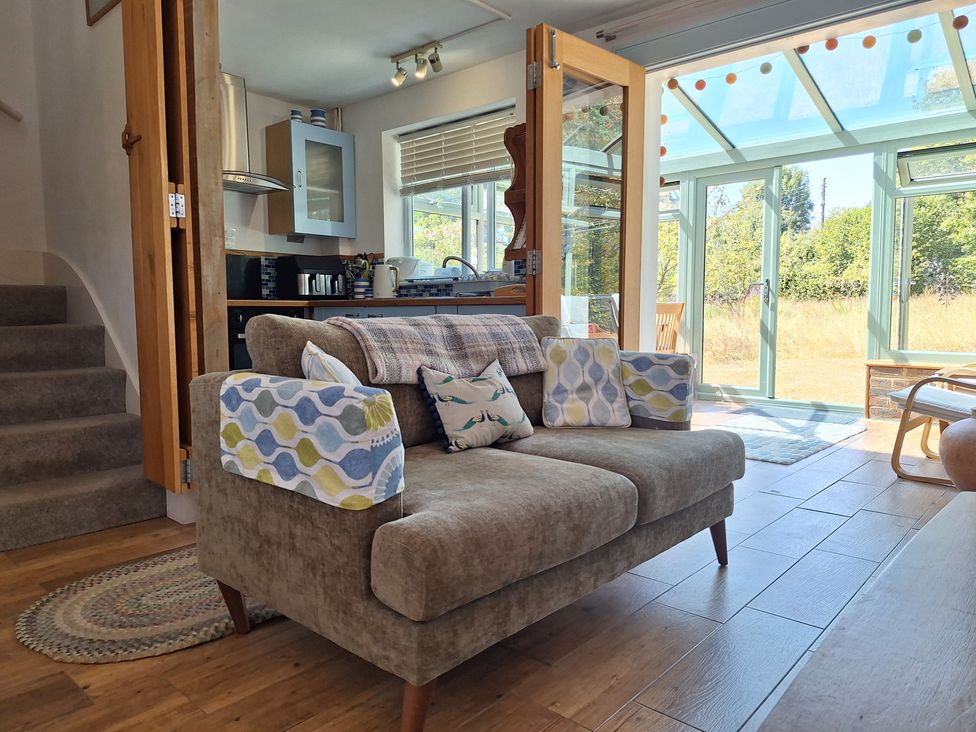 A living room with a sofa and kitchen visible at Wood Glen Cottage in Rushlake Green near Heathfield