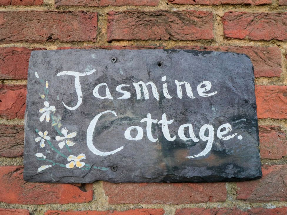 A slate sign with the text Jasmine Cottage on a brick wall