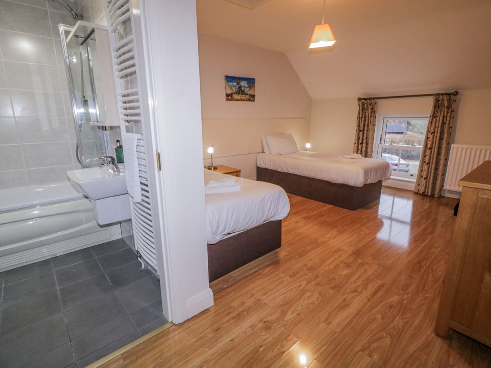 A bedroom with two beds and a bathroom featuring a bathtub at Foyle Cottage near Strabane