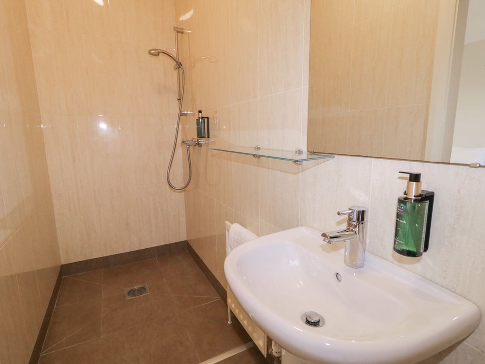 A bathroom with a shower, sink, towel, and soap dispenser at Derg Cottage