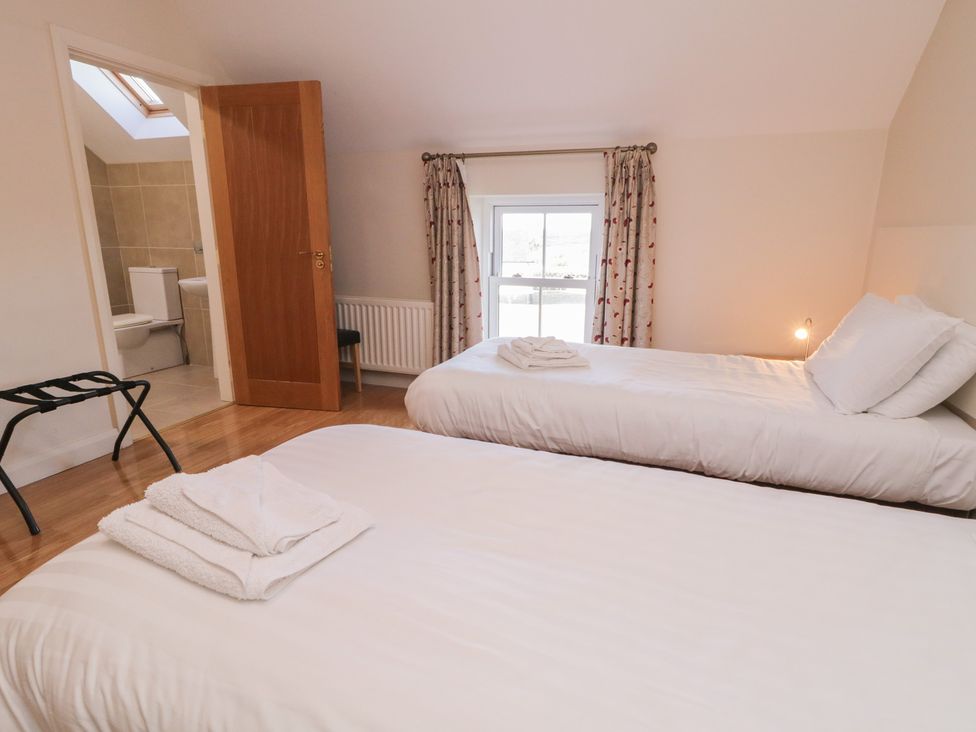A bedroom with two beds and a door leading to a bathroom at Finn Cottage