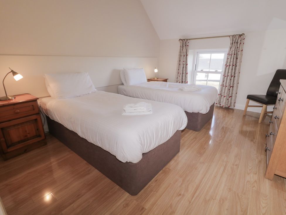 A bedroom with two beds, a nightstand, lamp, and a window at Finn Cottage