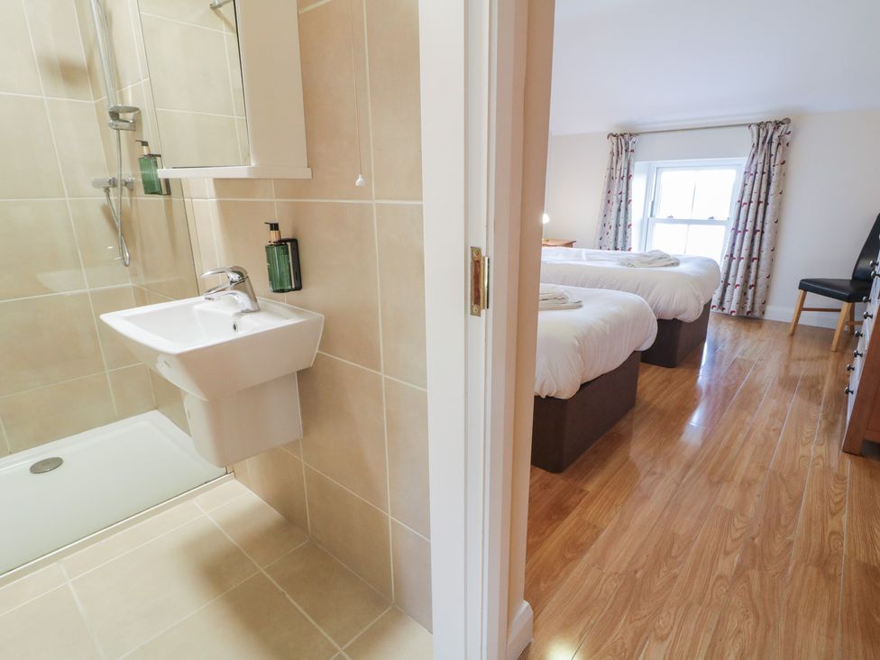 A bathroom with a shower and sink and a bedroom with twin beds at Finn Cottage