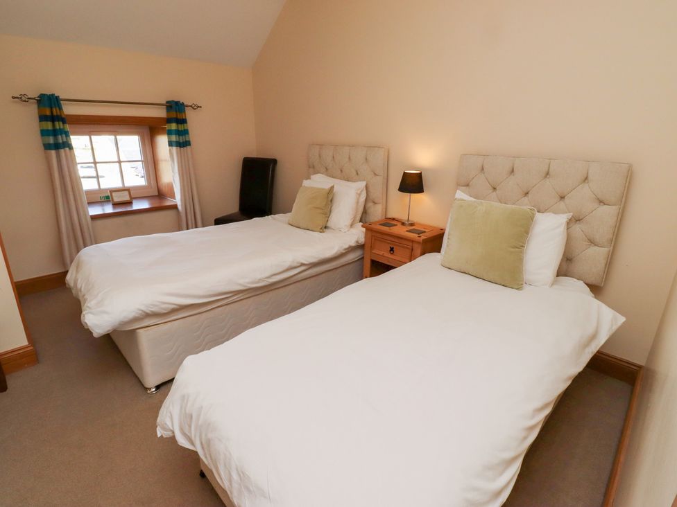 A bedroom with two single beds and a window at Granary Stone House in Embleton