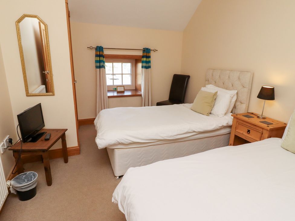 A bedroom with two beds and a television at Granary Stone House in Embleton