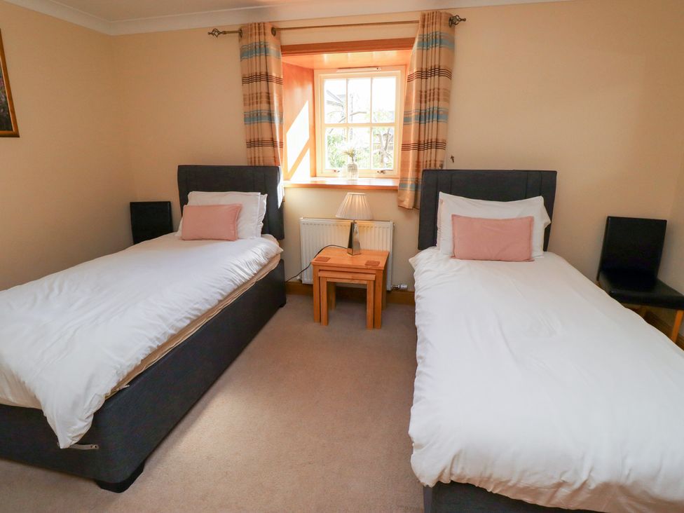 A bedroom with two beds and a table at Granary Stone House Embleton