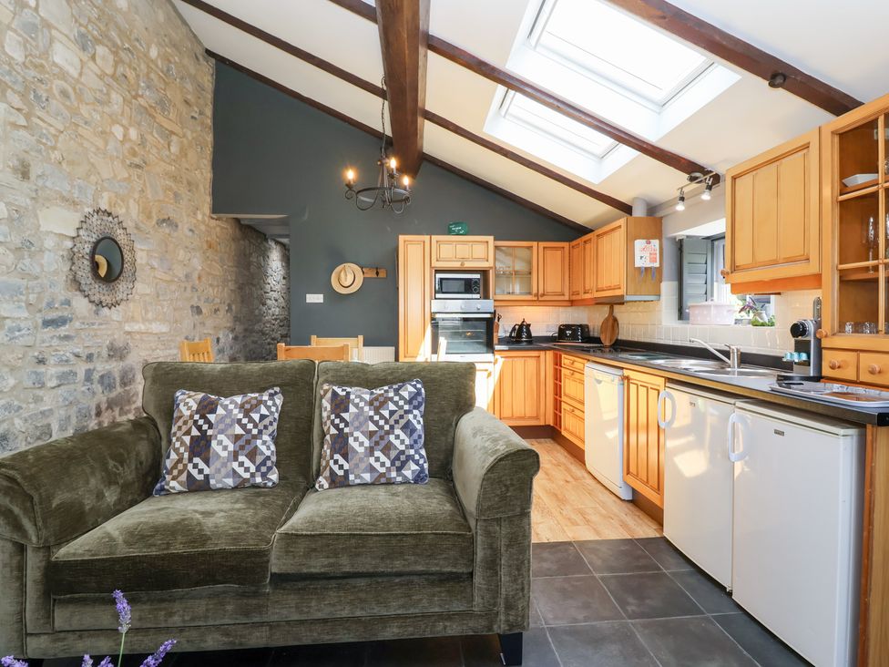 A kitchen with wooden cabinets and a sofa at Pear Tree Cottage Mark near Burnham-on-Sea