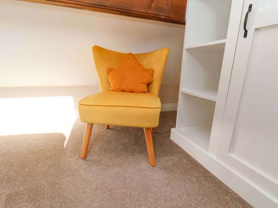 A reading nook with a yellow chair and cushion at Heather Croft in Robin Hood's Bay
