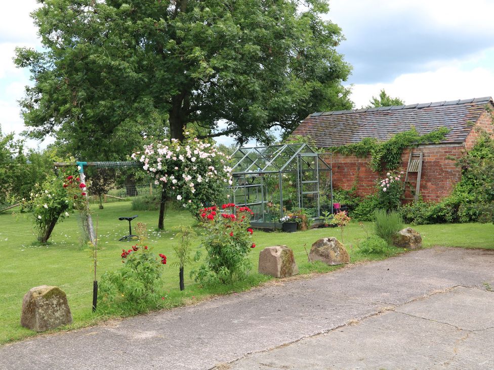 A garden with a greenhouse and flowers at Lake View Cottage Audley Brow near Market Drayton