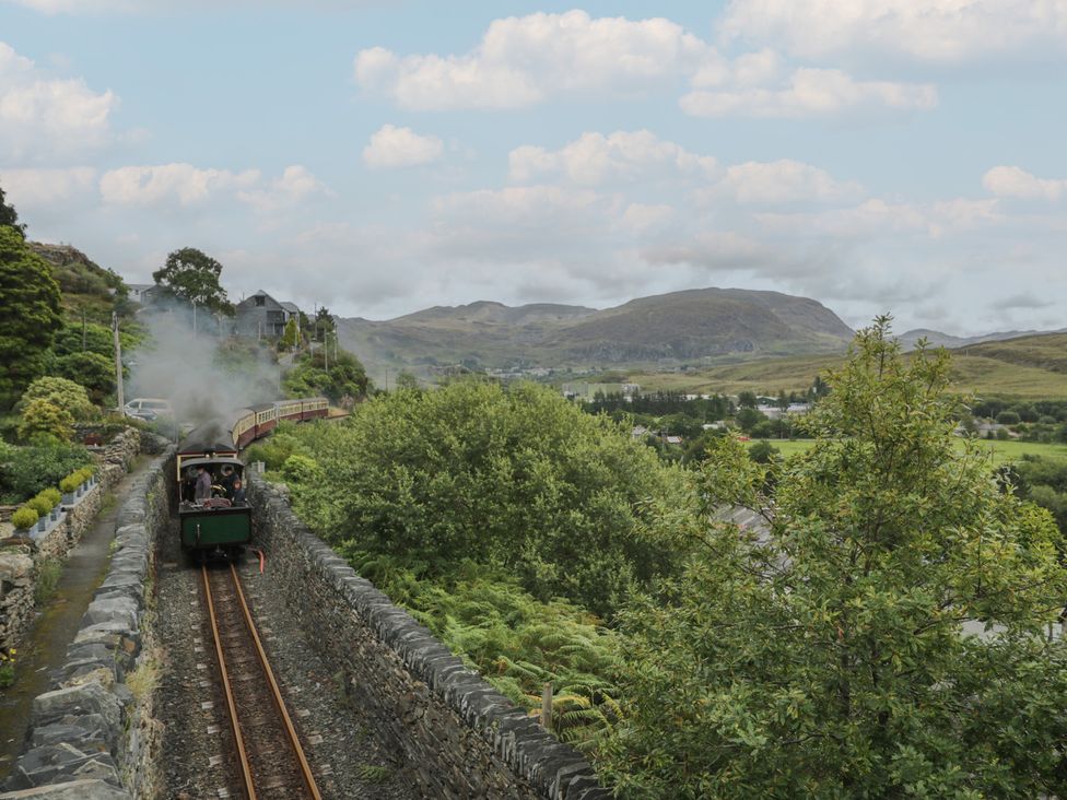 A steam train traveling along tracks surrounded by trees and mountains at Ty Gwynn Tanygrisiau