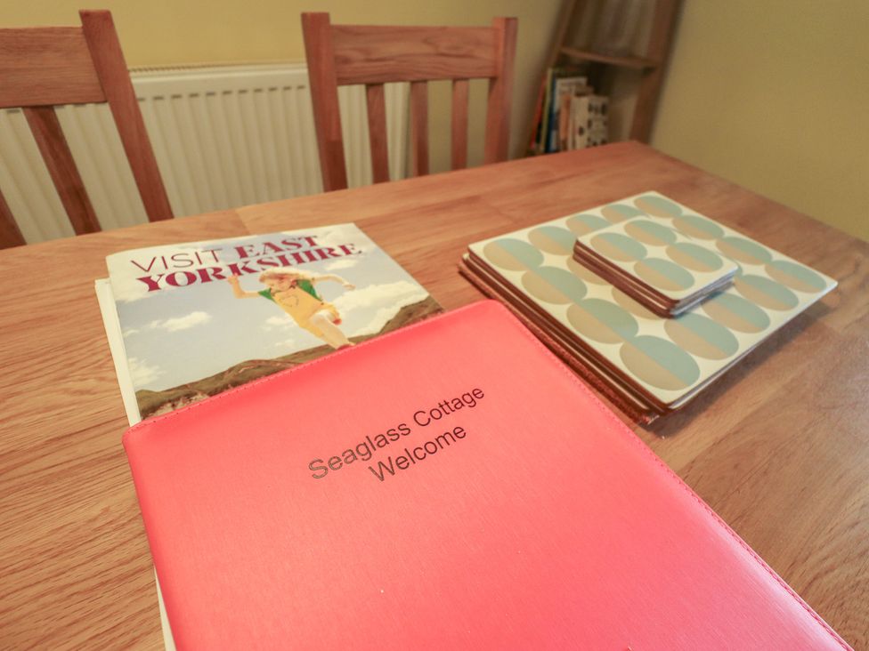 A dining table with a welcome book and coasters at Seaglass Cottage in Aldeburgh