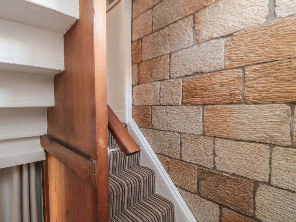 A staircase with a wooden railing and stone wall at Bulmers Cottage in Staithes