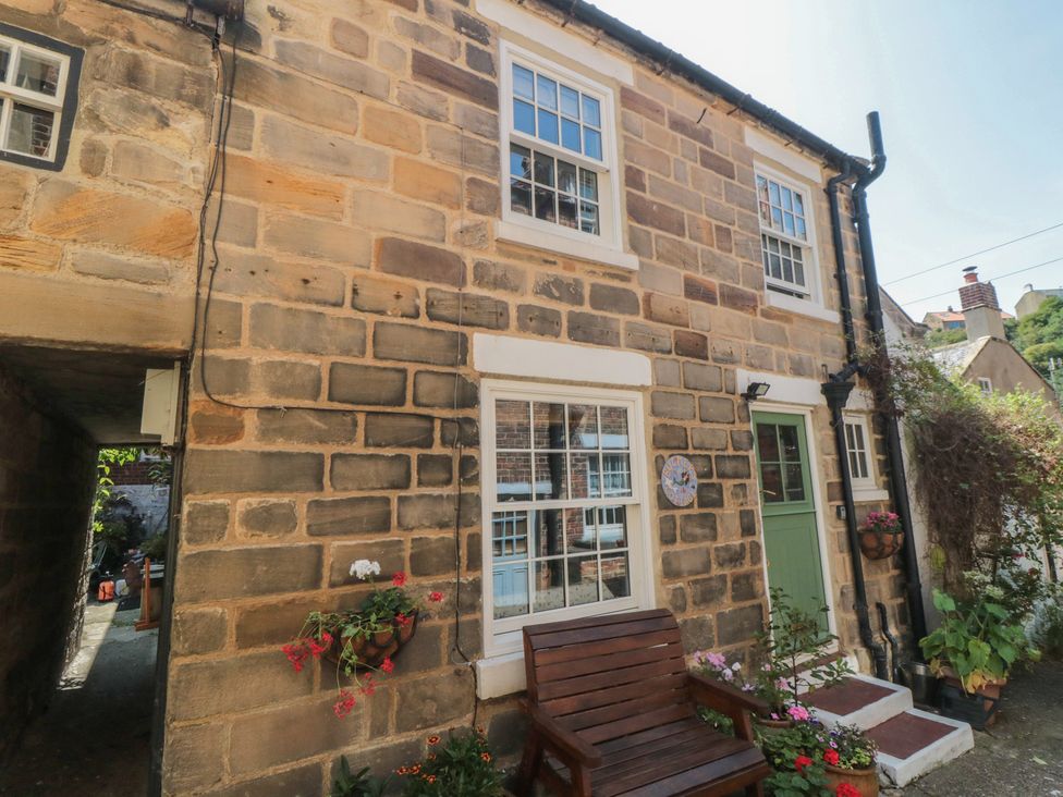 An outdoor area of a cottage with a stone wall and a bench at Bulmers Cottage in Staithes