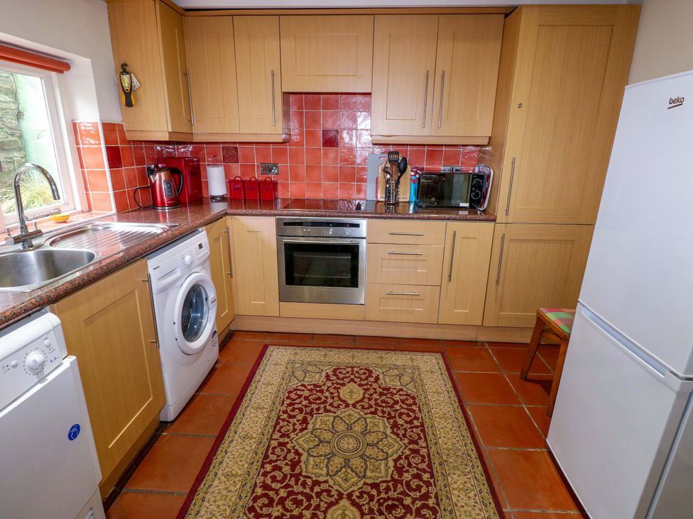 A kitchen with appliances and a rug at Milk Wood Cottage in Laugharne