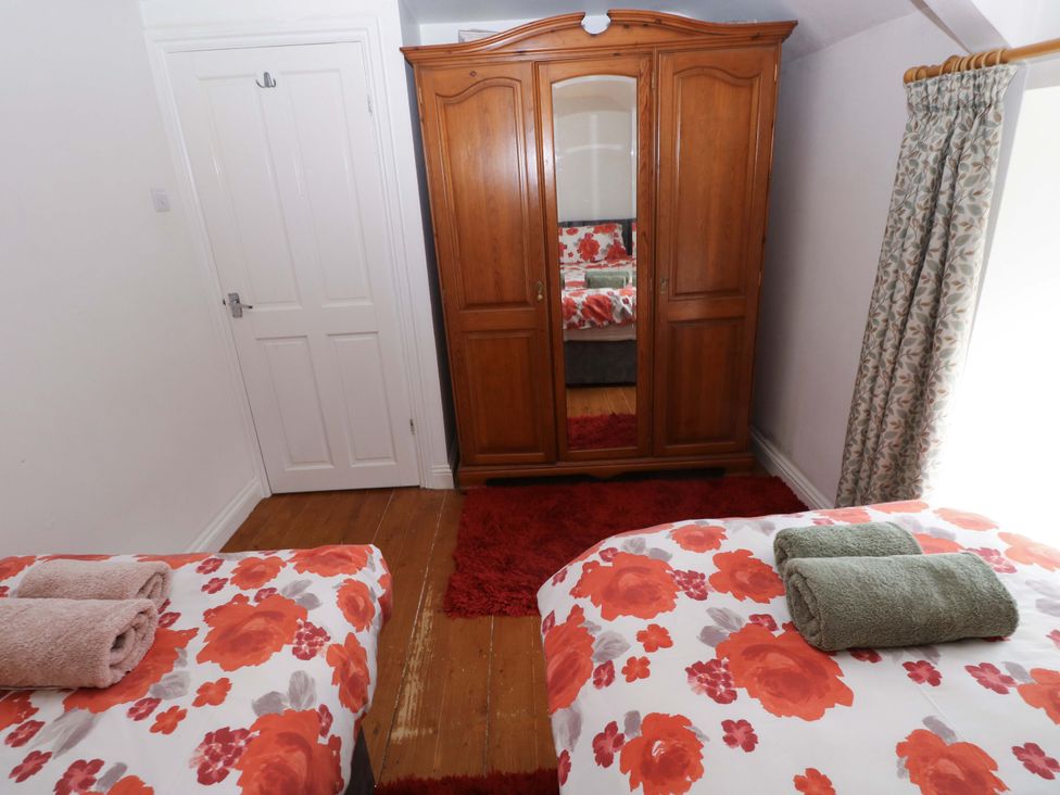 A bedroom with two beds and a wardrobe at Milk Wood Cottage in Laugharne