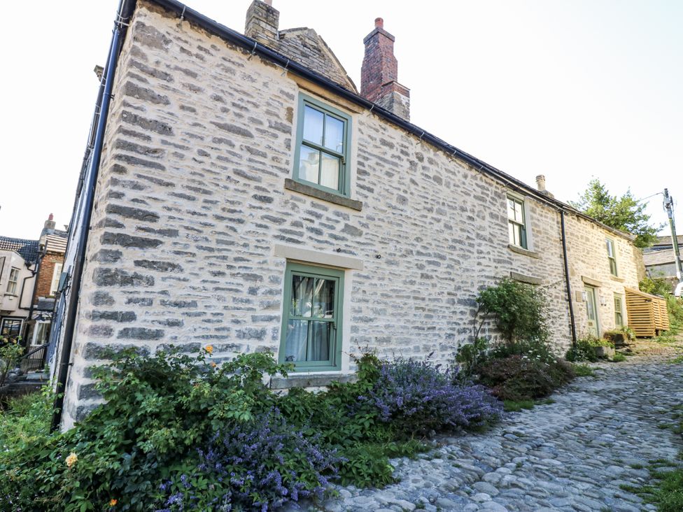 A stone house with windows and plants beside a cobblestone pathway at Castle Hill Cottage in Middleham, Wensleydale