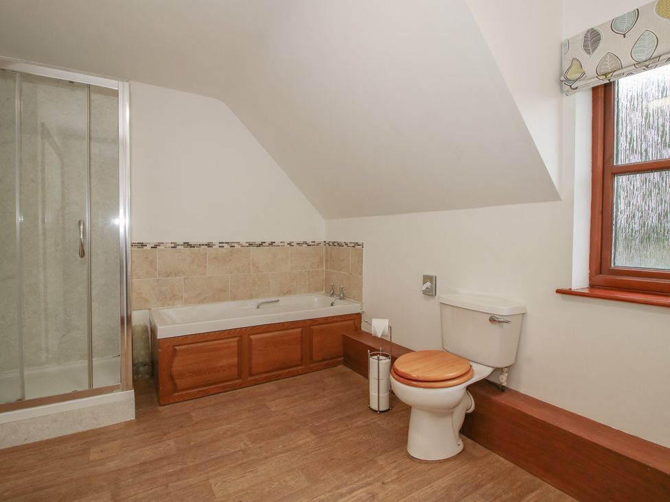 A bathroom with shower, bathtub, toilet, and window at Byne Brook Cottage in Strefford near Craven Arms