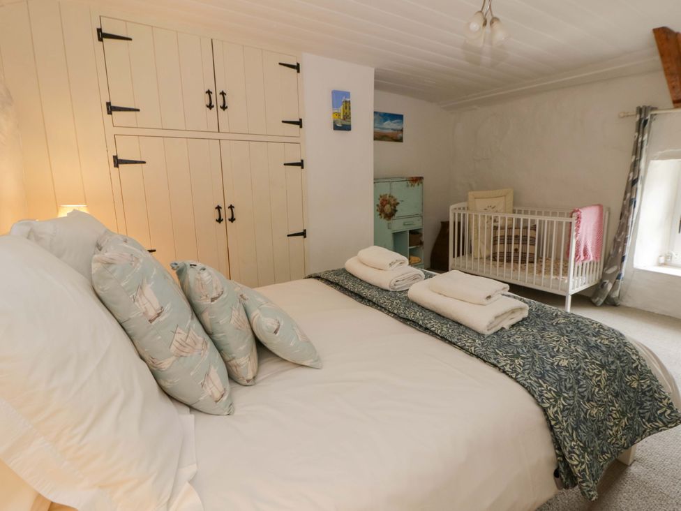 A bedroom with a bed, crib, and wardrobe at Fern Cottage in Aberporth