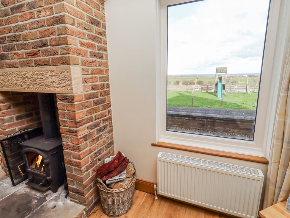 A living room with a fireplace and a view of a playground at Home Stead Cottage Embleton