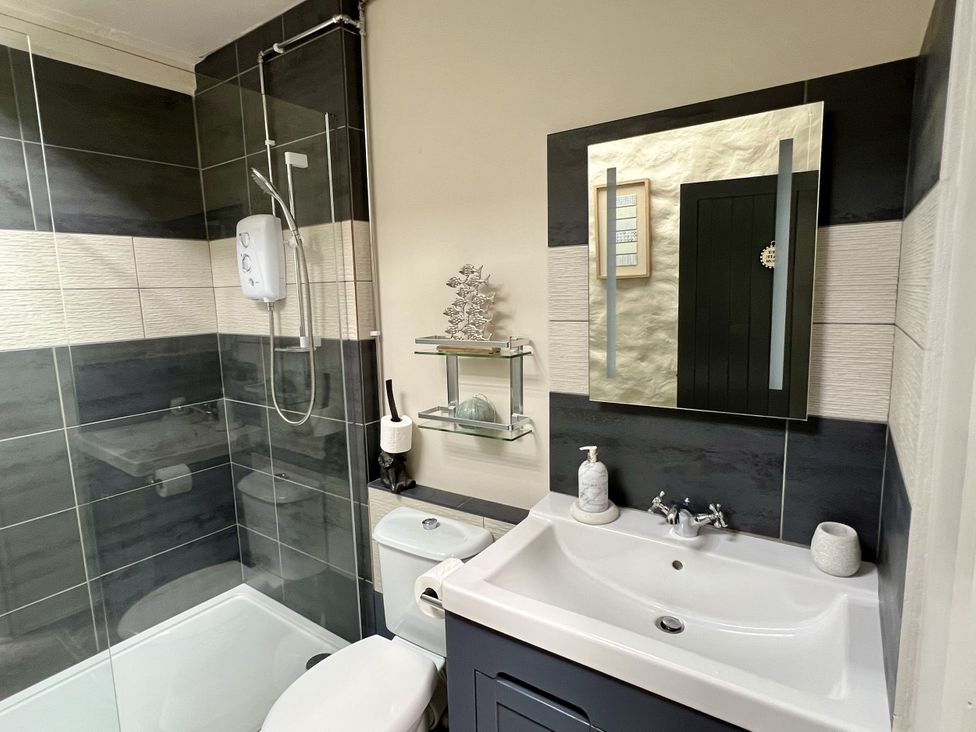 A bathroom featuring a shower, toilet, sink, and shelf at Swallows Cottage in Pembroke