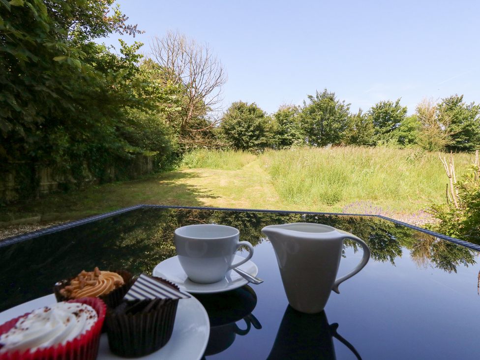 A table set with a cup, milk jug, and desserts overlooking a grassy area at Shepherd Oak in Upwey near Weymouth