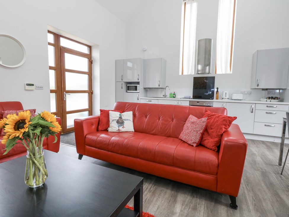 A living room with a red sofa and kitchen area at Everdene Upwey near Weymouth