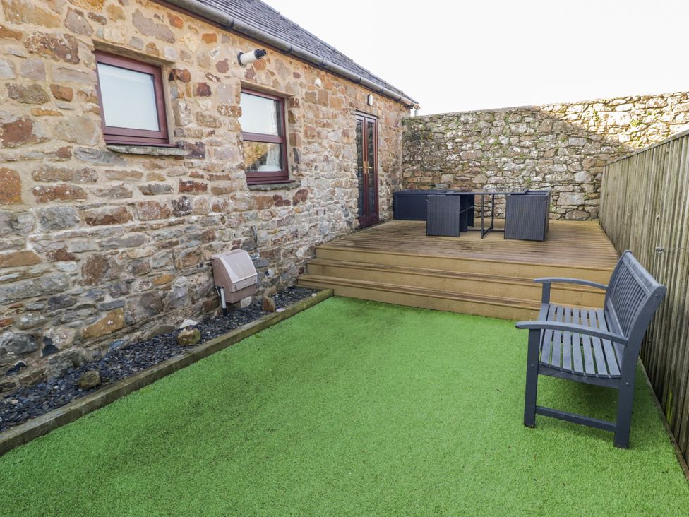 An outdoor area with a stone wall and patio furniture at Corner Cottage in Broad Haven