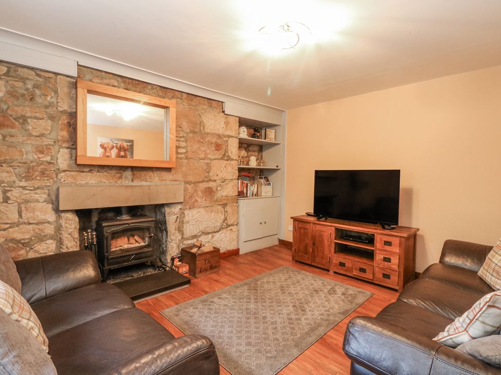A living room with a fireplace and television at Deskford Cottage in Nairn