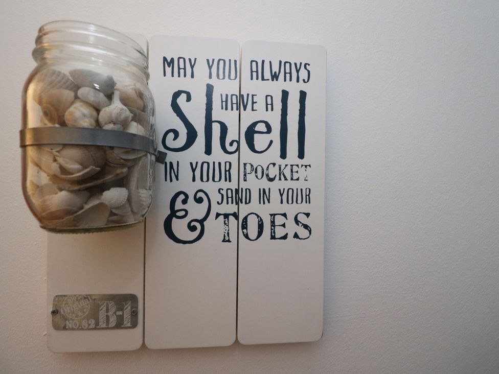 A wall decoration with a jar of shells and text at Deskford Cottage Nairn