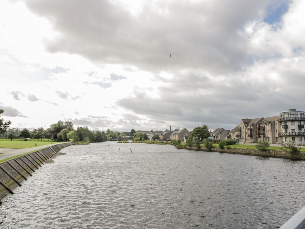 A view of a river with buildings and trees along the bank at Deskford Cottage Nairn