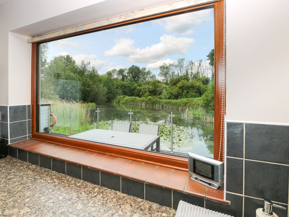 A kitchen view showing a table and chairs by the water at Dragonfly Lodge Whinburgh near Dereham