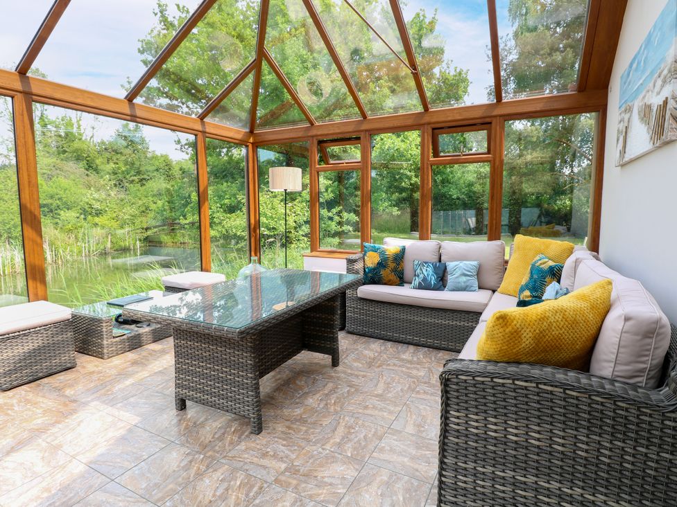 A conservatory with seating and outdoor views at Dragonfly Lodge Whinburgh near Dereham