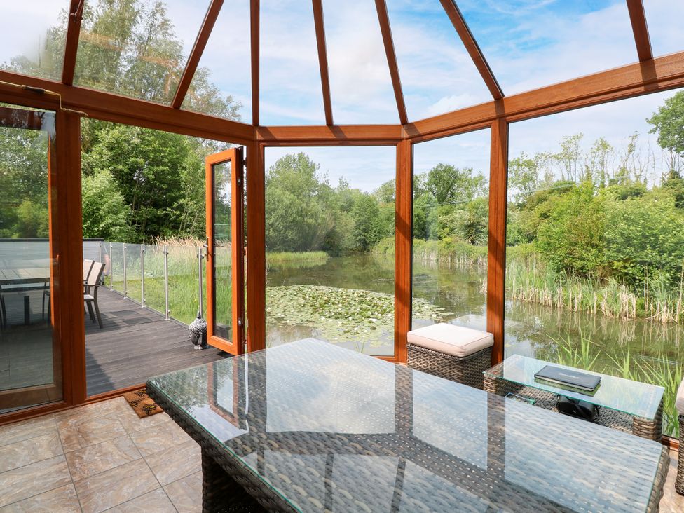 A conservatory with a glass table and view of water at Dragonfly Lodge Whinburgh near Dereham