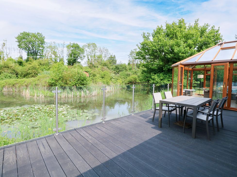 An outdoor seating area overlooking a pond at Dragonfly Lodge in Whinburgh near Dereham