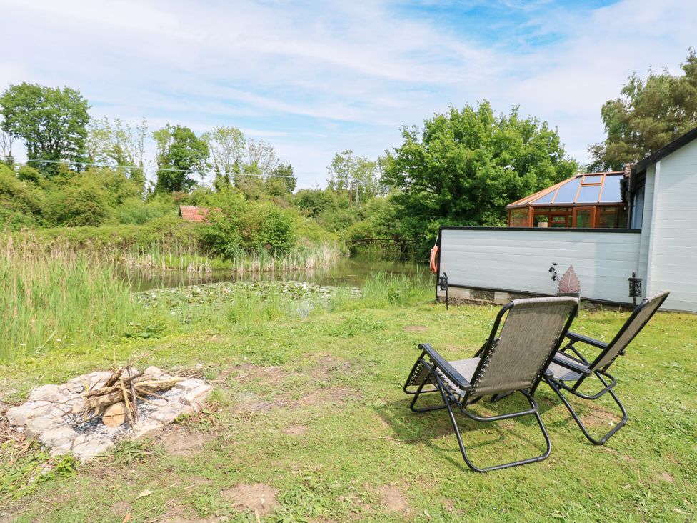 A garden with chairs and a fire pit near a pond at Dragonfly Lodge in Whinburgh near Dereham