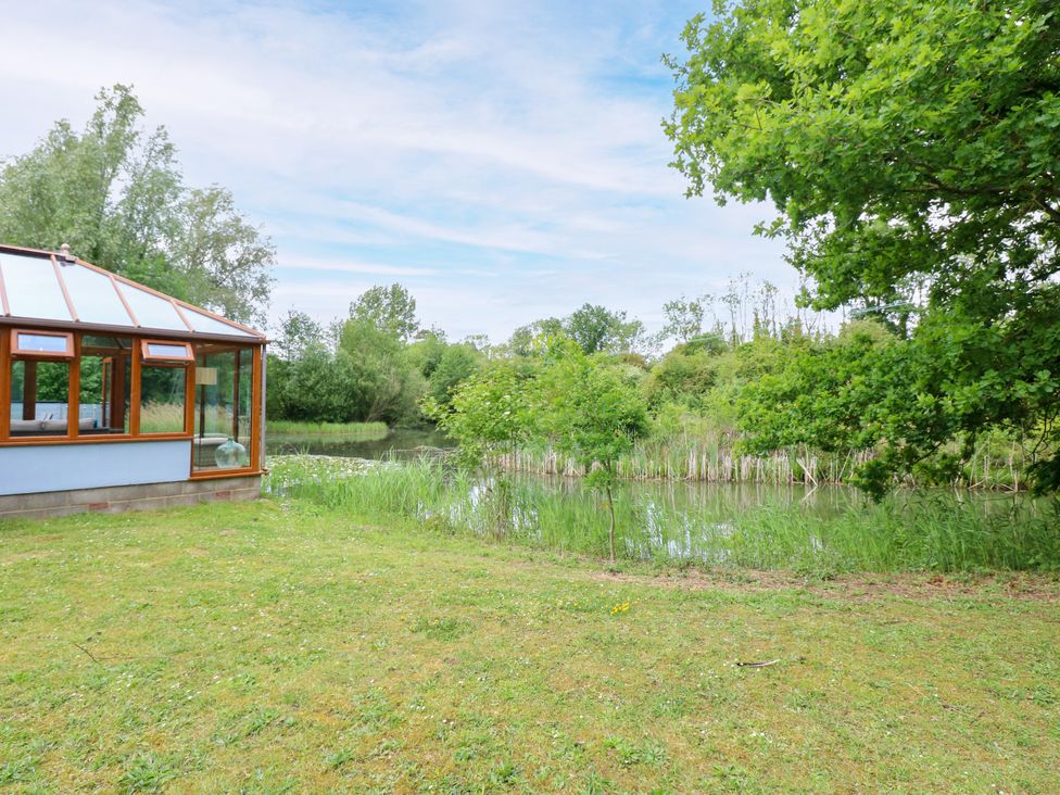 A garden area with a pond and a conservatory at Dragonfly Lodge in Whinburgh near Dereham