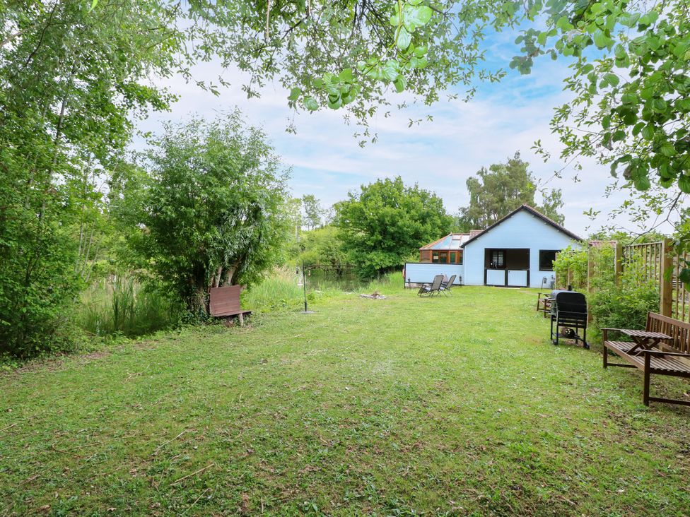 A garden with trees and chairs at Dragonfly Lodge in Whinburgh near Dereham