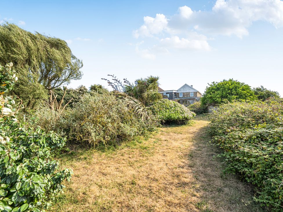 A pathway lined with bushes and trees leading to a house at Tregiffian Vean Sennen Cove