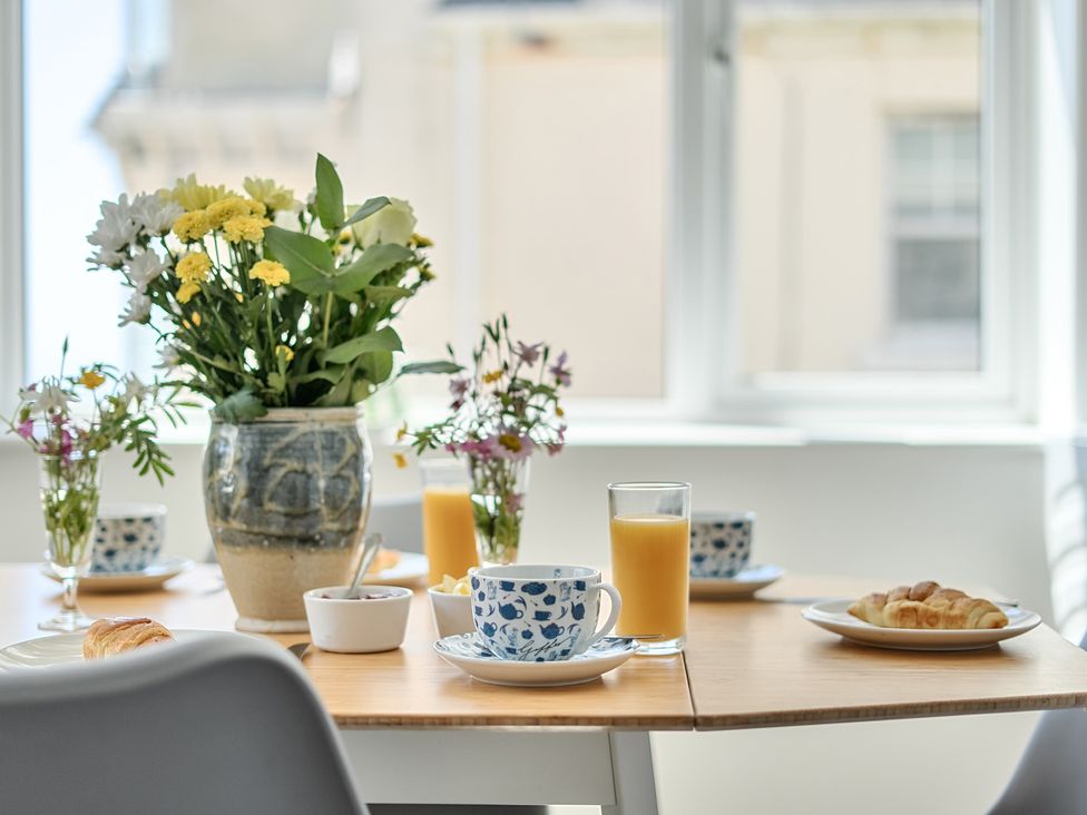A dining room table set with flowers, orange juice, croissant, and cups at Brook House in Sennen Cove near St Just