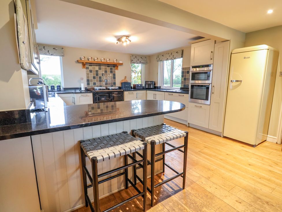 A kitchen with a bar counter and stools at Manor Wood in Farndon